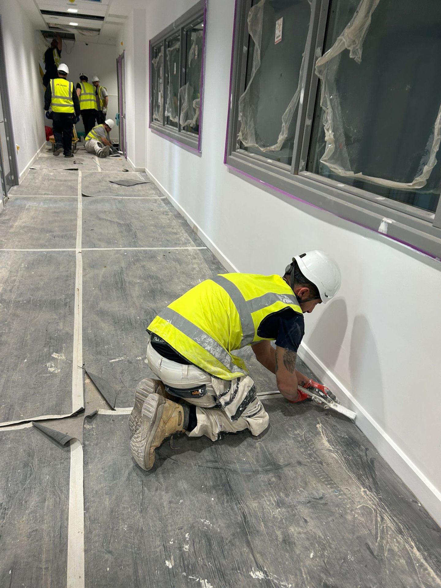 Bendrick decorator caulking skirting boards in a freshly painted clinic corridor